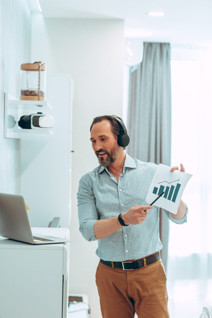 confident-young-man-pointing-graphic-chart-while-reporting-online-meeting-laptop-front-him