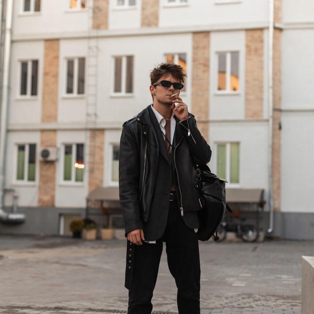 stylish-portrait-young-man-with-cigarette-fashion-sunglasses-cool-leather-black-jacket-with-trendy-backpack-city-street-urban-hipster-guy-wear-american-style-smokes-outdoors